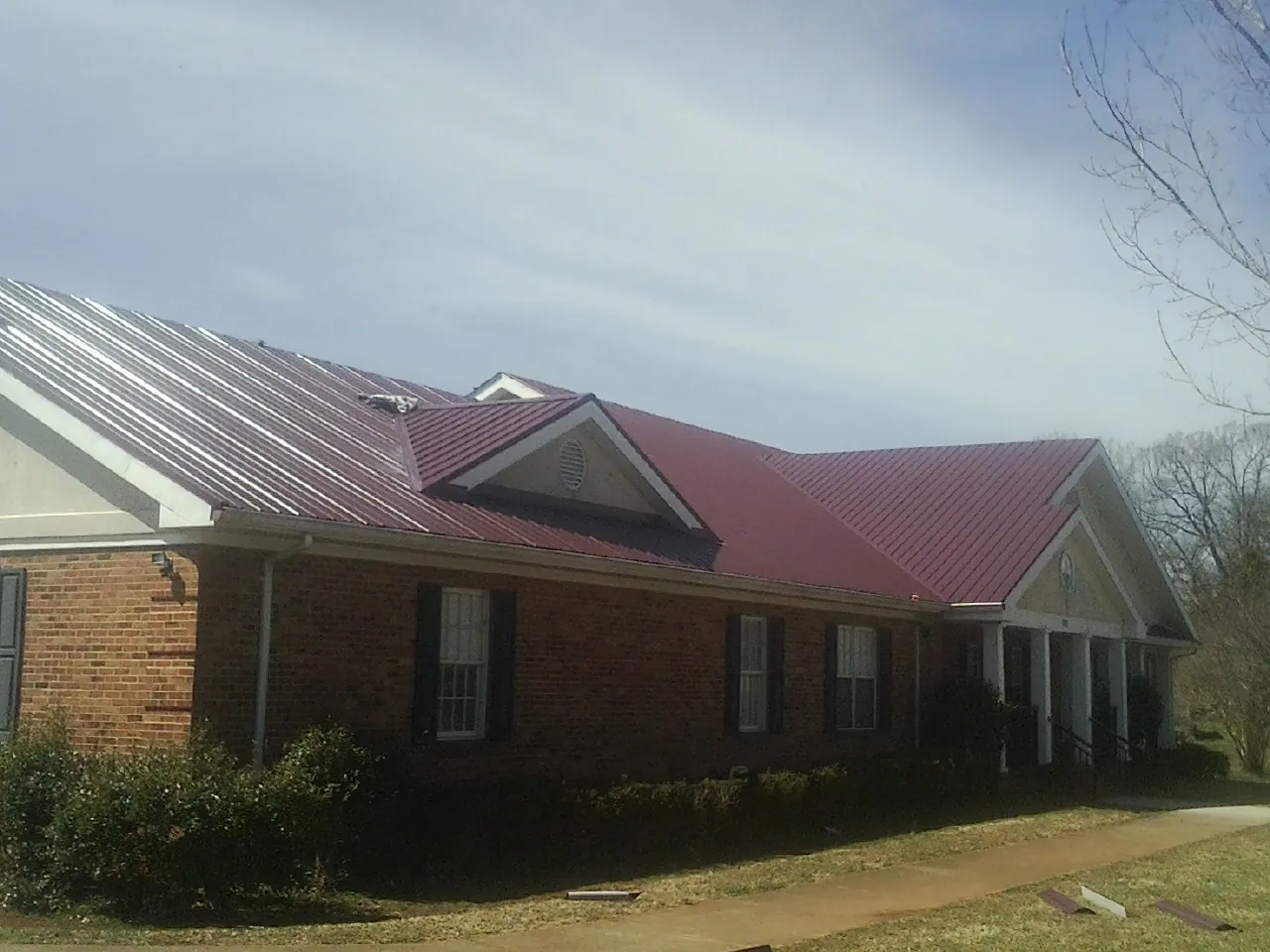 Red metal roof with gabled entries on a long brick building, from a Hail Damage Roof Repair job in Brattleboro