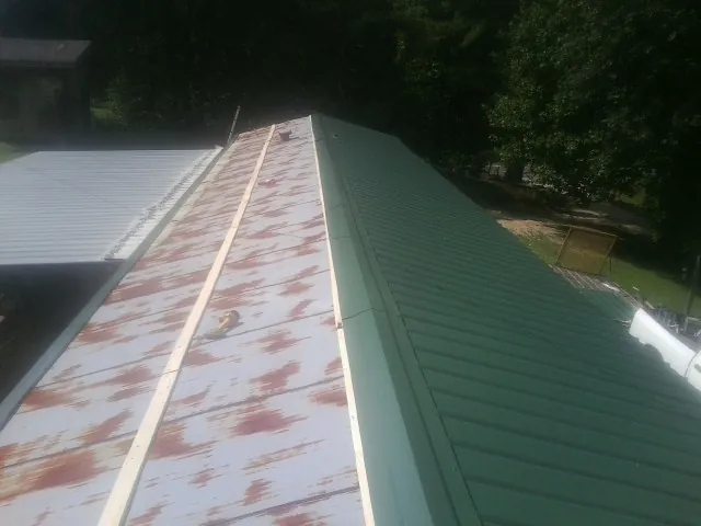 Old rusted panels beside newly installed green metal roofing — Wind Damage Roof Repair by Roofing Brothers in Brattleboro