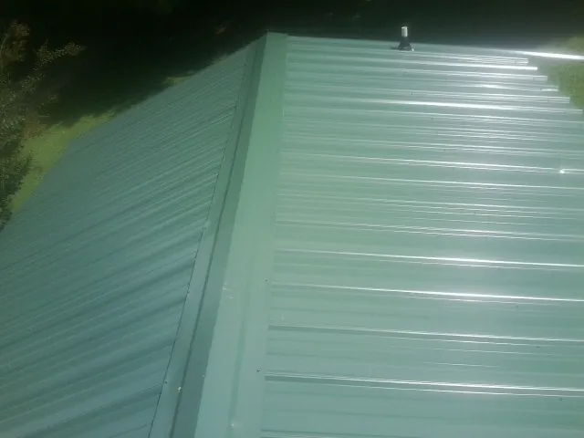 New green metal panels meeting at the ridge of a roof — Flat Roof Repair work by our crew in Brattleboro
