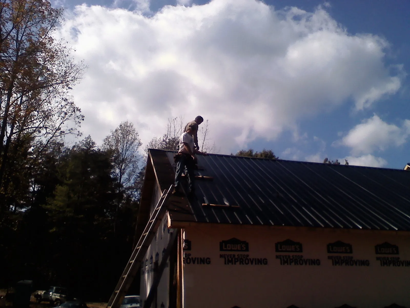 Roofer fastening dark metal panels high against a cloudy sky, from a Roof Inspection job in Brattleboro