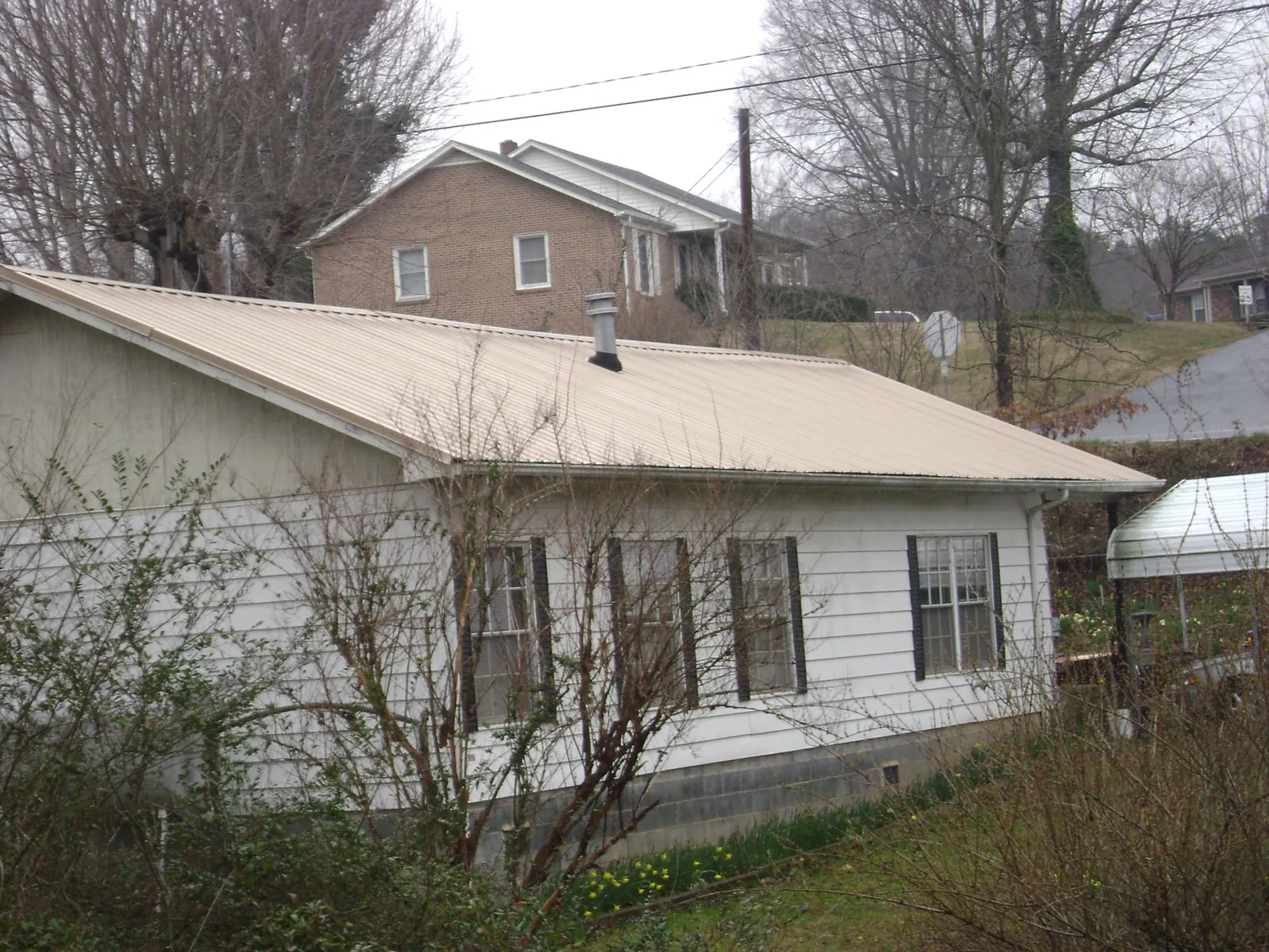 Tan metal roof on a white sided house set into a hillside — Commercial Roofing by Roofing Brothers in Brattleboro